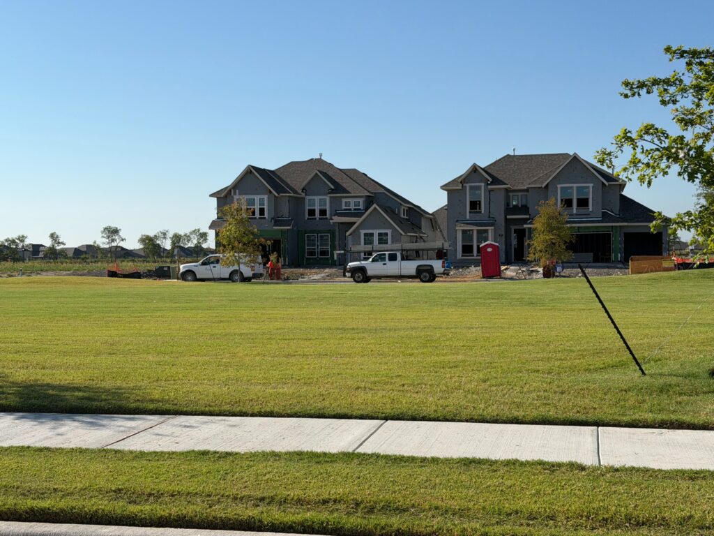 Two new two-story homes under construction behind an open lawn at Leonard Trails in Anna, Texas