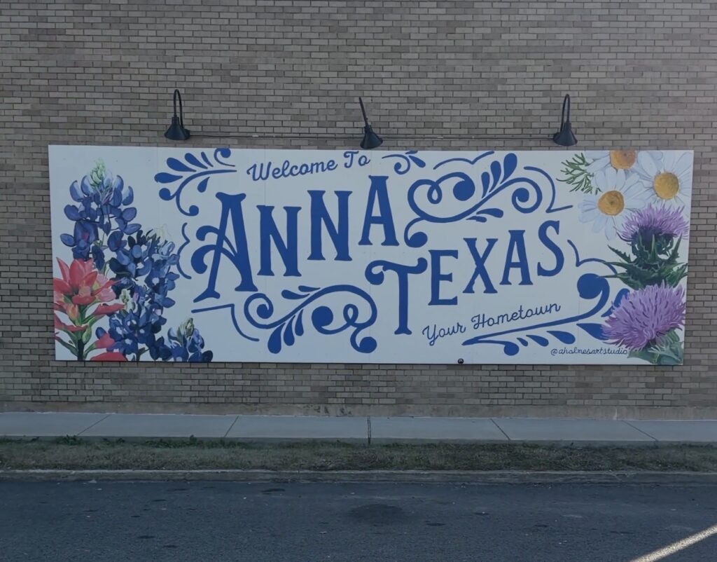Hand-painted Welcome to Anna, Texas Your Hometown mural with bluebonnets and wildflowers on a brick wall in downtown Anna, Texas
